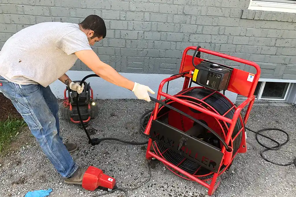 A Clark County Plumbing technician operating a red Maxliner hydro-jetting machine to clear a main sewer line from an exterior cleanout.