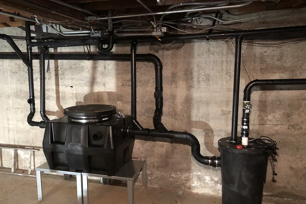 Professional installation of a new black ABS plastic drainage system and sump pump basin in a residential basement.