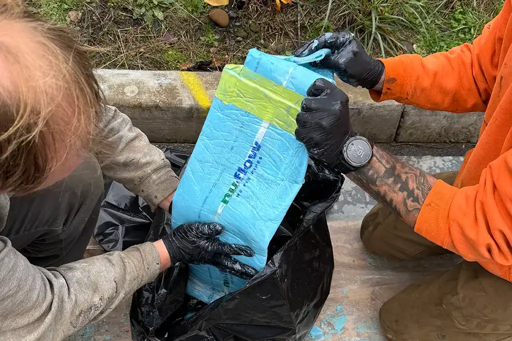 Close-up of technicians in black gloves carefully handling a blue NuFlow "We Fix Pipes" structural liner during a sewer rehabilitation project.