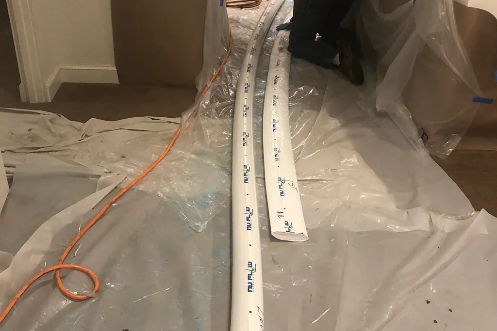 Long sections of white NuFlow pull-in-place structural lining laid out on protective plastic sheeting inside a residence, ready for installation.