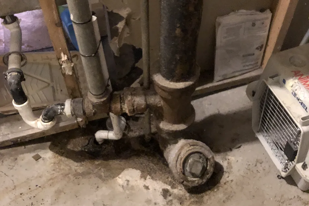 Close-up of heavily corroded and rusted cast iron sewer piping in a basement before being replaced by Clark County Plumbing.