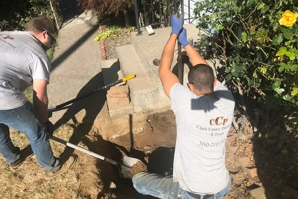 Technicians using a shovel and a post-hole digger to carefully excavate a small area for a trenchless pipe rehabilitation project.