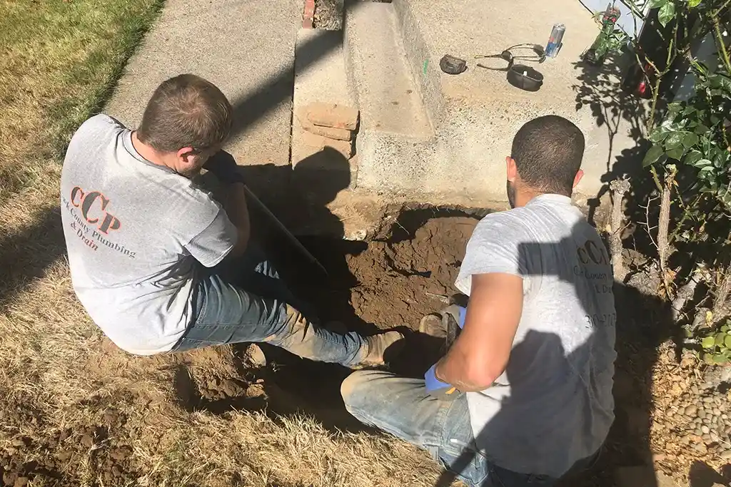 Two Clark County Plumbing & Drain technicians digging a targeted access hole for a trenchless sewer line repair in a front yard.