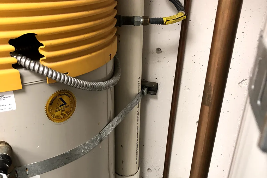 Close-up of a water heater’s safety strapping, gas line connection, and "Excellence in Design" certification gold seal.