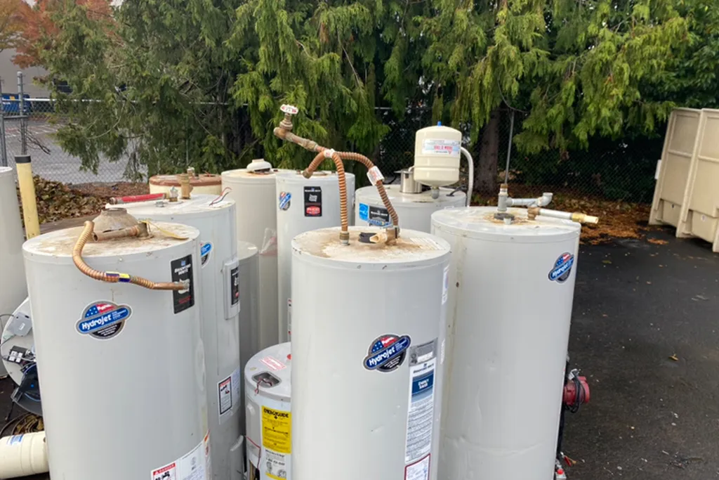 A collection of decommissioned old water heaters staged outdoors for recycling after replacement by Clark County Plumbing.