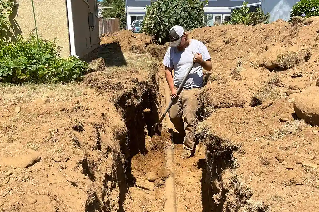 A Clark County Plumbing worker standing in a deep, narrow trench during a main sewer line repair project.