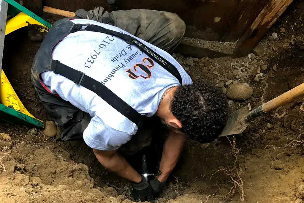An overhead view of a technician working inside an excavation to secure a pipe fitting.