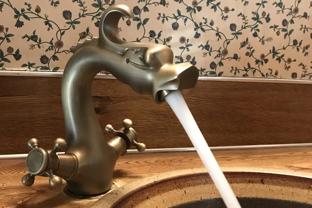 An elegant, ornate bronze dragon-shaped bathroom faucet running water into a ceramic vessel sink.