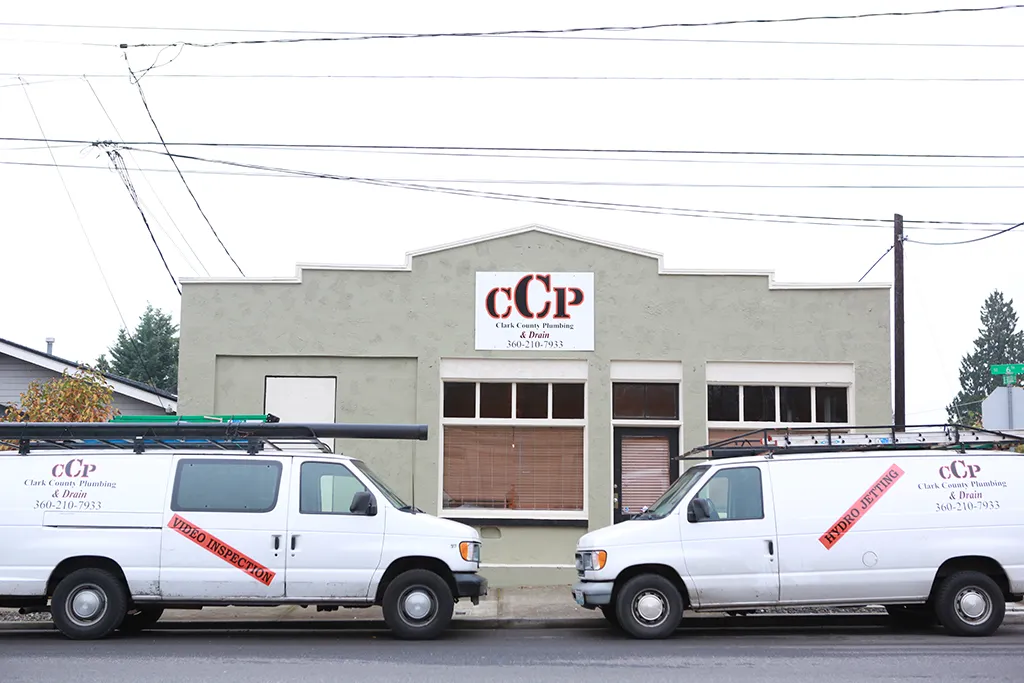 Two white service vans parked in front of the Clark County Plumbing & Drain storefront office.