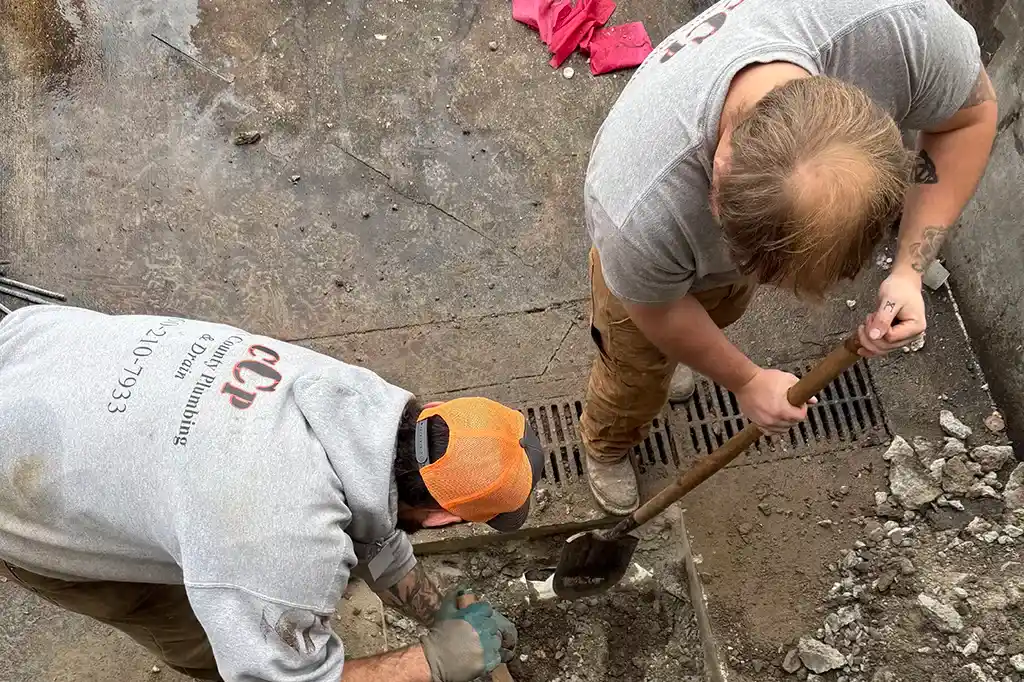 Two technicians working together to clear debris and prepare a ground area for a plumbing repair.