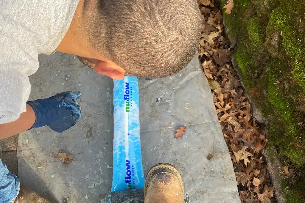 Two Clark County Plumbing technicians kneeling on a driveway, carefully preparing a long white NuFlow structural pipe liner on a protective plastic sheet.